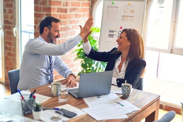 Two business professionals high fiving in front of a desk.